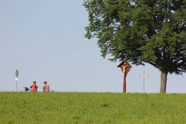 Haziran ayında Güney Almanya çok güneşli bir günde ağaç ağaç yakınındaki dini haç ile sürüş bisikletçi görmek