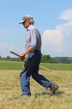 Haziran ayında Güney Almanya çok güneşli bir günde saman, araçları ve mavi pantolon gün sona ermeden işi için çalışkan çiftçi haying görüşürüz