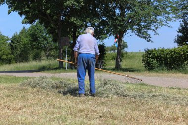 Haziran ayında Güney Almanya çok güneşli bir günde saman, araçları ve mavi pantolon gün sona ermeden işi için çalışkan çiftçi haying görüşürüz
