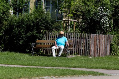 Haziran ayında Güney Almanya çok güneşli bir günde kıdem bayanlar ve baylar bir bankta oturan veya nordic walking sopalarla yürüyüş cloister Park görmek