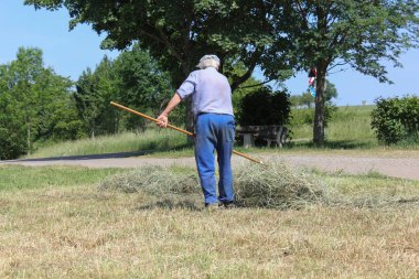 Haziran ayında Güney Almanya çok güneşli bir günde saman, araçları ve mavi pantolon gün sona ermeden işi için çalışkan çiftçi haying görüşürüz