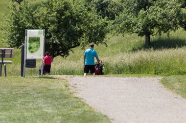 çok güneşli bir Güney Almanya'da golf çim yeşil gördüğünüz ve bayrak ve oyuncular ve kum alanları ve golfplace çevresinde yolu olan mahkeme