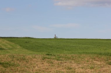 Haziran ayında Güney Almanya çok güneşli bir günde ağaç ağaç yakınındaki dini haç ile sürüş bisikletçi görmek