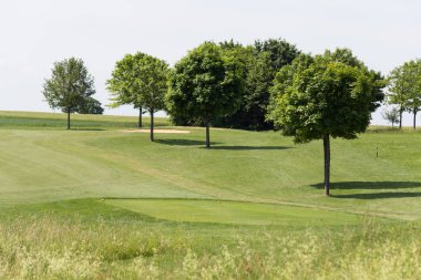 çok güneşli bir Güney Almanya'da golf çim yeşil gördüğünüz ve bayrak ve oyuncular ve kum alanları ve golfplace çevresinde yolu olan mahkeme