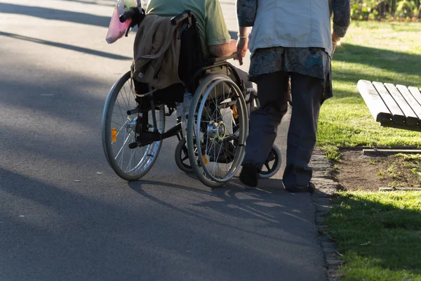 on a evening in june in south germany in center park of a historical city you see couple with wheelchair moving through shadow giving park