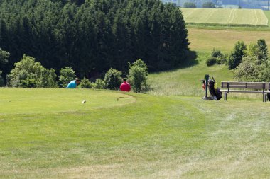 çok güneşli bir Güney Almanya'da golf çim yeşil gördüğünüz ve bayrak ve oyuncular ve kum alanları ve golfplace çevresinde yolu olan mahkeme