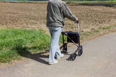 on a way beside green field and blue sky rollator with senior  man on a sunny day end of summer september at rural landscape near city of stuttgart clipart