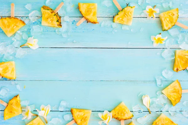 Pineapple popsicle sticks with ice on wood plank blue color. frame layout  summer fruit backgrond concept, top view