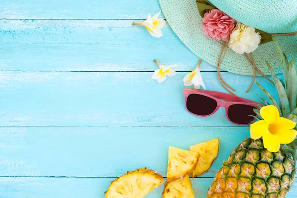 Tropikal meyve kavramı. Ananas, çiçek, güneş gözlüğü ve ahşap üzerine hasır şapka mavi renk plank. Yaz tatil arka plan ve üst tasarımını görüntüle