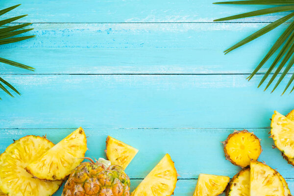 Tropical fruit composition. Pineapple slices and palm leaves  on wood plank blue color. Summer vacation background concept. top view, copy space