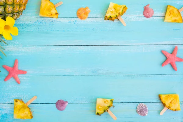 Yaz konsepti. Ananas dondurma çubukları, deniz yıldızı ve kabukları ahşap tahta mavi renk üzerinde çerçeve yaptı. tatil arka plan. üstten görünüm