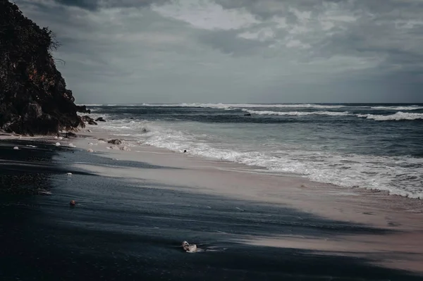 Beautiful balinese landscape. Ocean black sandy coast with white sea foam and dark huge rocks. Bali Island, Indonesia.