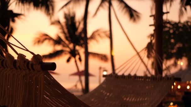 Mysiga vita hängmatta på stranden mot en bakgrund av poolen, havet och solnedgång. — Stockvideo