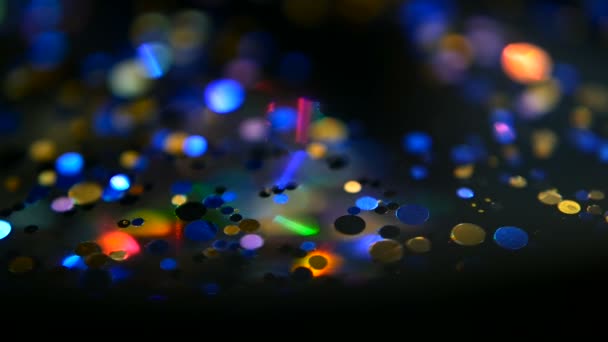 Confettis scintillants multicolores déconcentrés, fond noir. vacances abstraites festives bokeh spots lumineux . — Video