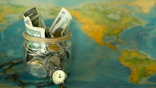 Reizen begroting concept. Geld voor vakantie opgeslagen in glazen pot op de wereld kaart achtergrond — Stockvideo