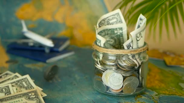 Концепция бюджета путешествия. Деньги, сэкономленные на отдыхе в стеклянной банке на фоне карты мира — стоковое видео