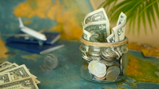 Concepto de presupuesto de viaje. Dinero ahorrado para vacaciones en frasco de vidrio en el fondo del mapa del mundo — Vídeos de Stock