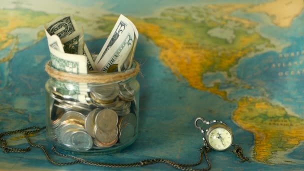 Reizen begroting concept. Geld voor vakantie opgeslagen in glazen pot op de wereld kaart achtergrond — Stockvideo