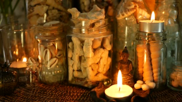 Γυάλινη φιάλη γεμάτη με κοχύλια, κοράλλια, θαλάσσιες αντικείμενα με κερί φώτα, λουλούδια plumeria, κάθεται ο Βούδας για διακόσμηση — Αρχείο Βίντεο