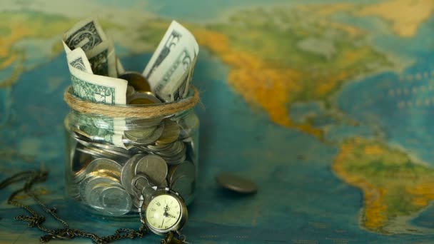 Koncepcja budżetu podróży. Pieniądze Zapisano na wakacje w szklanym słoju na tle mapy świata — Wideo stockowe