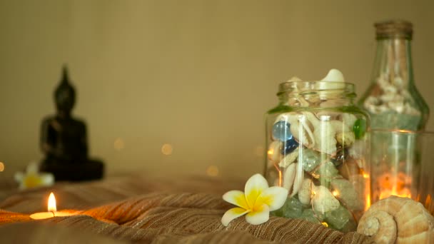 Bouteille en verre remplie de coquillages, coraux, articles marins avec des bougies, fleurs plumeria, bouddha assis pour la décoration — Video