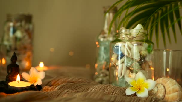 Bottiglia di vetro piena di conchiglie, coralli, oggetti marini con luci a candela, fiori di plumeria, buddha seduto per l'arredamento — Video Stock