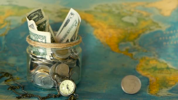 Conceito de orçamento de viagem. Dinheiro guardado para férias em frasco de vidro no fundo do mapa mundial — Vídeo de Stock