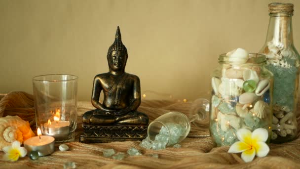 Стеклянная бутылка, наполненная ракушками, кораллами, морскими предметами со свечами, цветами плюмерии, сидящий Будда для декора — стоковое видео