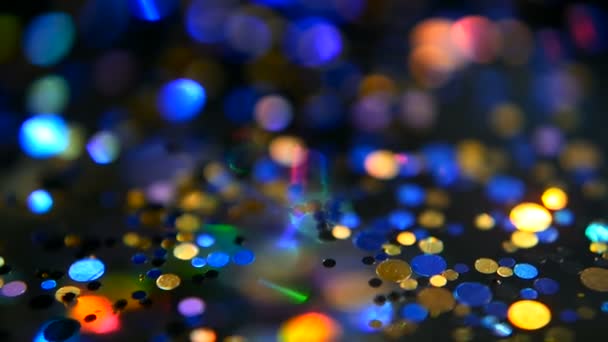 Intreepupil glinsterende veelkleurige glitter confetti, zwarte achtergrond. Vakantie abstracte feestelijke bokeh licht vlekken. — Stockvideo