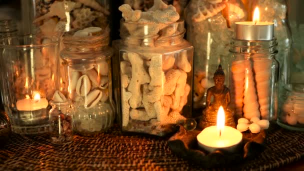 Garrafa de vidro cheia de conchas, corais, itens marinhos com luzes de vela, flores de plumeria, buddha sentado para decoração — Vídeo de Stock