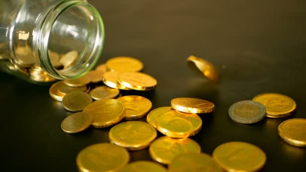 Close-up still life with gold coins on black table and rotating penny. Yellow coins fell out from jar. — Stock Video