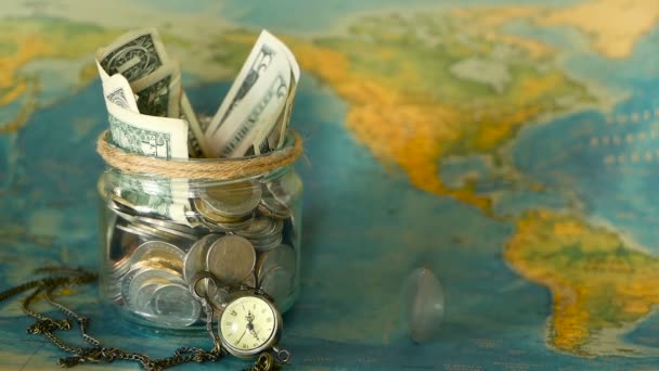 Conceito de orçamento de viagem. Dinheiro guardado para férias em frasco de vidro no fundo do mapa mundial — Vídeo de Stock