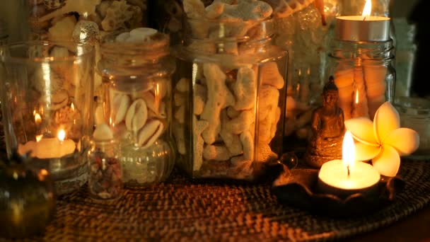 Bottiglia di vetro piena di conchiglie, coralli, oggetti marini con luci a candela, fiori di plumeria, buddha seduto per l'arredamento — Video Stock