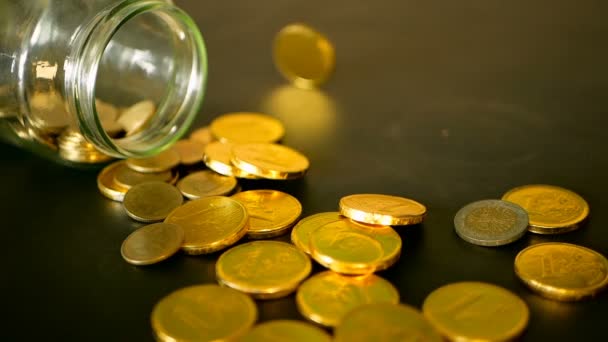 Close-up still life with gold coins on black table and rotating penny. Yellow coins fell out from jar. — Stock Video