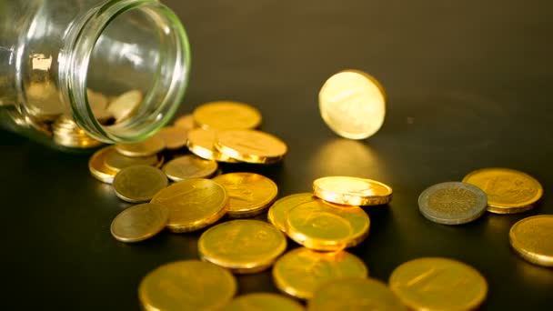 Bodegón de primer plano con monedas de oro en la mesa negra y centavo giratorio. Las monedas amarillas cayeron del frasco . — Vídeo de stock