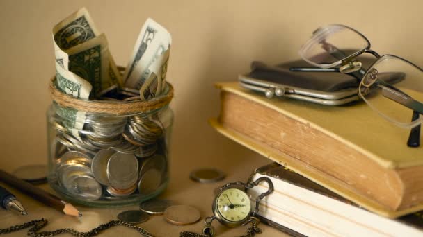 书里装满了硬币和钞票的玻璃便士罐子。学费或教育经费的概念。奖学金资金. — 图库视频影像