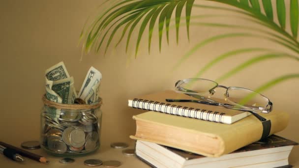 Bøger med glas penny krukke fyldt med mønter og sedler. Undervisnings- eller uddannelsesfinansieringskoncept. Stipendiebeløb . – Stock-video