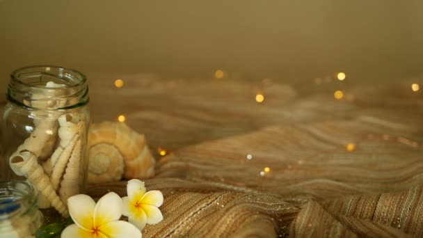 Стеклянная банка, наполненная ракушками, кораллами, морскими предметами с боке огни, plumeria frangipani цветы для декора — стоковое видео