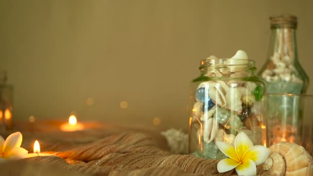 Botella de vidrio llena de conchas marinas, corales, artículos marinos con velas, plumeria frangipani flores para la decoración — Vídeo de stock