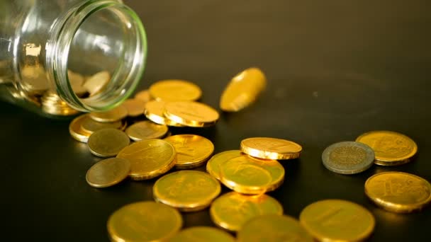 Bodegón de primer plano con monedas de oro en la mesa negra y centavo giratorio. Las monedas amarillas cayeron del frasco . — Vídeo de stock
