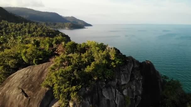 Pohled shora letecké dron exotický ráj tropické pobřežním útesu s lávovými kameny pokryté zelenou džungli deštného pralesa a coconun dlaně vymyje klidný oceán nebo na moři, ostrov Koh Prangan, Thajsko. — Stock video