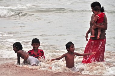 Hikkaduwa, Sri Lanka - 18 Aralık 2011 yetişkin etnik kadın okyanus su dalgalar halinde sıçramasına çocuklar grup ile görüntüleyin. Okyanus suda oynarken çocuklu kadınla