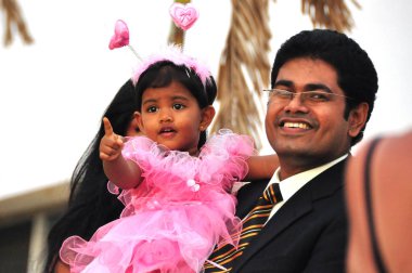 Hikkaduwa, Sri Lanka - 18 Aralık 2011 neşeli yetişkin etnik Hintli adam sevimli küçük kız pembe kıyafet açık havada duran ve smilingaway taşıyan takım elbiseli. Aile