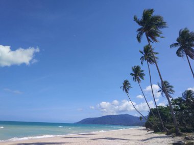Beyaz kumlu sahili ve sakin mavi deniz. pastoral tropik cenneti egzotik ada peyzaj yemyeşil ağaçlar ve dağlar ve gökyüzü arka plan üzerinde okyanus dalgalanan sessiz ile. Sessiz sörf, su üstünde düşük görünümü