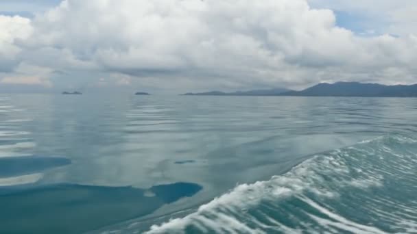 小さなボートと曇りの日の穏やかな海の青い波の泡。牧歌的な熱帯の水辺。空は海のはかなりの水の表面に反映されます。風のない天気, — ストック動画