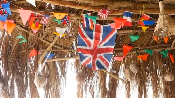 Bandeiras nacionais decorativas de diferentes países penduradas em cordas em bangalô tropical de madeira. Interior de bar rasta exótico. Casa de praia de verão na ilha Koh Phangan, Tailândia — Vídeo de Stock