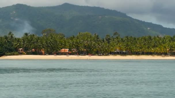 Sandy beach with small traditional thai style huts and calm ocean, Koh Samui Island, Thailand. Green coconut palms on the shore and a mountain behind. Idyllic tropical exotic paradise waterscape, — Stock Video