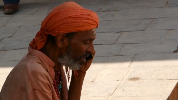 KATHMANDU,ネパール- 12 10月2018電話を持つシニア民族の男.サイドビューでは、頭の中で高齢者のインド人男性の通りの距離を探して電話で話す。パシュパティナート・ヒンドゥー教寺院付近の火葬. — ストック動画