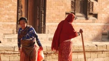 BHAKTAPUR, KATHMANDU, NEPAL - 18 Ekim 2018 Asyalı erkek ve yaşlı kadın ulusal kıyafetler içinde mutlu bir şekilde gülümsüyor, alıyor. Vatandaşlar günlük yaşam, depremden sonra antik doğu şehri.