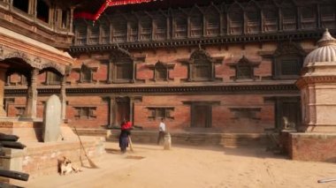 BHAKTAPUR, KATHMANDU, NEPAL - 18 Ekim 2018 Tapınak merdivenlerini süpüren yaşlı kadın. Hindu tapınağının merdivenlerini silip süpüren renkli kumaşlı yaşlı kadın. Durbar kraliyet sarayı.